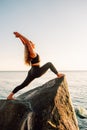 Young long-haired woman in warrior pose from yoga standing on a big stone in water with her hands up. Sunset, relaxation Royalty Free Stock Photo