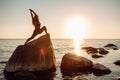 Young long-haired woman in warrior pose from yoga standing on a big stone in water with her hands up. Sunset, relaxation Royalty Free Stock Photo