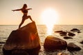 Young long-haired woman in warrior pose from yoga standing on a big stone in water. Sunset, relaxation, meditation Royalty Free Stock Photo