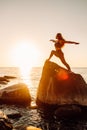 Young long-haired woman in warrior pose from yoga standing on a big stone in water. Sunset, relaxation, meditation Royalty Free Stock Photo