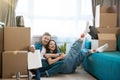 Young lovely couple man and woman looking satisfied sitting on the floor hugging during moving to new apartment unpacking boxes Royalty Free Stock Photo