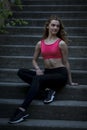 Young pretty sportive girl is sitting on the steps on the late summer evening looking down smiling