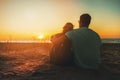 young lovers couple sitting in sand on beach at romantic golden sunset