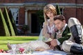 Young lovers dressed in vintage clothing sitting on picnic blanket. Gentleman reading to his lover from a book of poems Royalty Free Stock Photo