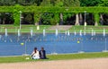 Young lovers a guy and a girl sit by the pond and look at the fountain