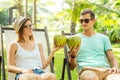 Young loving couple drink coconut while sitting under palms in deck chair lounge resort Royalty Free Stock Photo