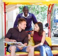 Young loving couple enjoying tour of city on trishaw with affable African American driver