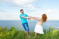 Couple dancing in grass over lake and sky background. Shot of attractive young red hair woman holding hands of the bearded man. Royalty Free Stock Photo