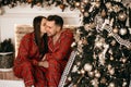 Young loving couple man and woman in red pajamas are sitting near the Christmas tree and fireplace Royalty Free Stock Photo