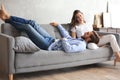 Young loving couple relaxing on sofa together, husband lying on wife legs resting on couch