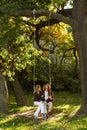 Young loving couple riding on wooden swing in park