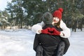 Young loving couple on winter forest background, girl keeps hands in heart shape sign. Sunny frosty day