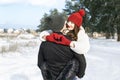 Young loving couple in winter forest. Happy young woman keeps hands in heart shape and embrace her boyfriend. Sunny day