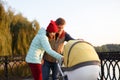 A young loving family walks by the lake with a stroller. Smiling parents couple with baby pram in autumn park look into cariage. L Royalty Free Stock Photo