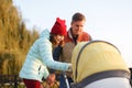 A young loving family walks by the lake with a stroller. Smiling parents couple with baby pram in autumn park look into cariage. L Royalty Free Stock Photo