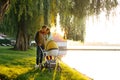 A young loving family walks by the lake with a stroller. Smiling parents couple with baby pram in autumn park. Love, parenthood, f