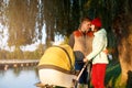 A young loving family walks by the lake with a stroller. Smiling parents couple with baby pram in autumn park. Love, parenthood, f Royalty Free Stock Photo