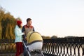 A young loving family walks by the lake with a stroller. Smiling parents couple with baby pram in autumn park. Love, parenthood, f Royalty Free Stock Photo