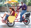 Young loving couple enjoying tour of city on trishaw with affable African American driver