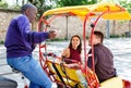 Young loving couple enjoying tour of city on trishaw with affable African American driver