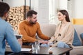 Young loving wife supporting her depressed husband during psychotherapy session with counselor, free space Royalty Free Stock Photo