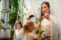 Young loving mom making ponytail to little preschool daughter and adult sister on background in living room. Mother Royalty Free Stock Photo