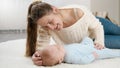 Young loving mother stroking and talking to her baby boy lying on carpet at living room. Concept of family happiness and Royalty Free Stock Photo