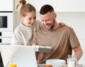 Young loving wife making surprise for husband on Birthday while standing in kitchen at home