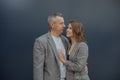 Young loving woman and handsome aged gray haired partner embracing and looking to each other, gray background. Romantic Royalty Free Stock Photo