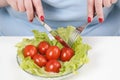 Young lush fat woman in casual blue clothes on a white background at the table and eats a vegetable salad with tomatoes Royalty Free Stock Photo