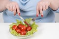 Young lush fat woman in casual blue clothes on a white background at the table and eats a vegetable salad with tomatoes Royalty Free Stock Photo