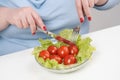 Young lush fat woman in casual blue clothes on a white background at the table and eats a vegetable salad with tomatoes Royalty Free Stock Photo