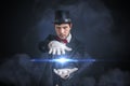 Young magician man is showing bright ball that levitates. Black background Royalty Free Stock Photo