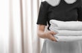 Young maid holding stack of fresh towels in hotel room, closeup Royalty Free Stock Photo