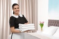 Young maid holding stack of fresh towels in hotel room. Royalty Free Stock Photo