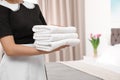 Young maid holding stack of fresh towels in hotel room Royalty Free Stock Photo