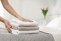 Young maid putting stack of fresh towels on bed in hotel room Royalty Free Stock Photo