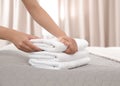 Young maid putting stack of fresh towels on bed in hotel room Royalty Free Stock Photo