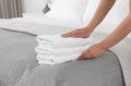 Young maid putting stack of fresh towels on bed Royalty Free Stock Photo