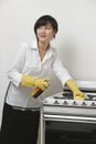 Young maidservant looking away while cleaning stove against gray background
