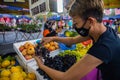 Young Malasian woman checks the quality of the grapes before buying. The girl is wearing face mask because of the virus crisis. Royalty Free Stock Photo