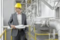 Young male architect holding rolled up blueprints by industrial machinery Royalty Free Stock Photo