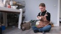 A young male artist with innate physical limitations paints pottery in an art studio