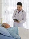 A young male asian doctor wearing white lab coat with stethoscope holding black tablet in his hands stand smiling in front of old Royalty Free Stock Photo