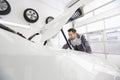 Young male automobile mechanic examining car engine in repair shop