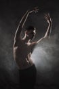 A young male ballet dancer with black leggings and a naked torso performs dance moves against a gray grunge background Royalty Free Stock Photo