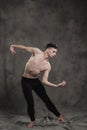 A young male ballet dancer with black leggings and a naked torso performs dance moves against a gray grunge background Royalty Free Stock Photo