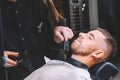 Young male barber shaves the client`s beard with a electric trimmer. Young bearded man getting haircut by hairdresser at barber Royalty Free Stock Photo