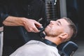 Young male barber shaves the client`s beard with a electric trimmer. Young bearded man getting haircut by hairdresser at barber Royalty Free Stock Photo