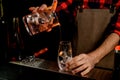 Young male barman carefully pours cocktail from mixing cup into transparent glass. Royalty Free Stock Photo